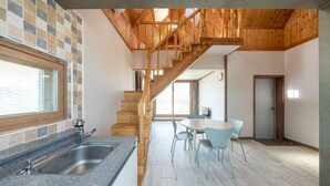 Una cocina con encimera de granito, pileta de acero inoxidable y una escalera de madera que lleva a un comedor con una mesa redonda y sillas.