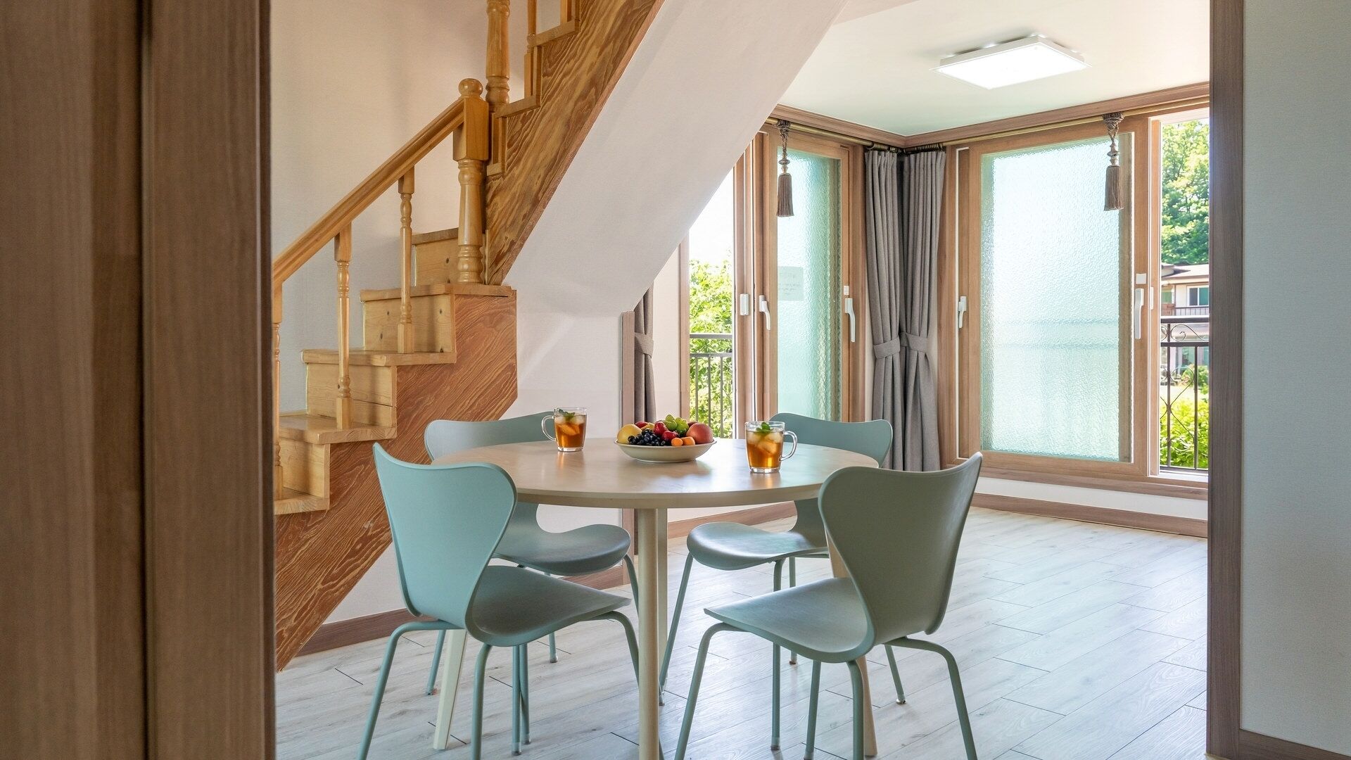 Un coin repas avec une table ronde, quatre chaises, un escalier et de grandes fenêtres.