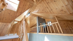 A wooden interior with a sloped ceiling, a balcony with wooden railings, and a window.