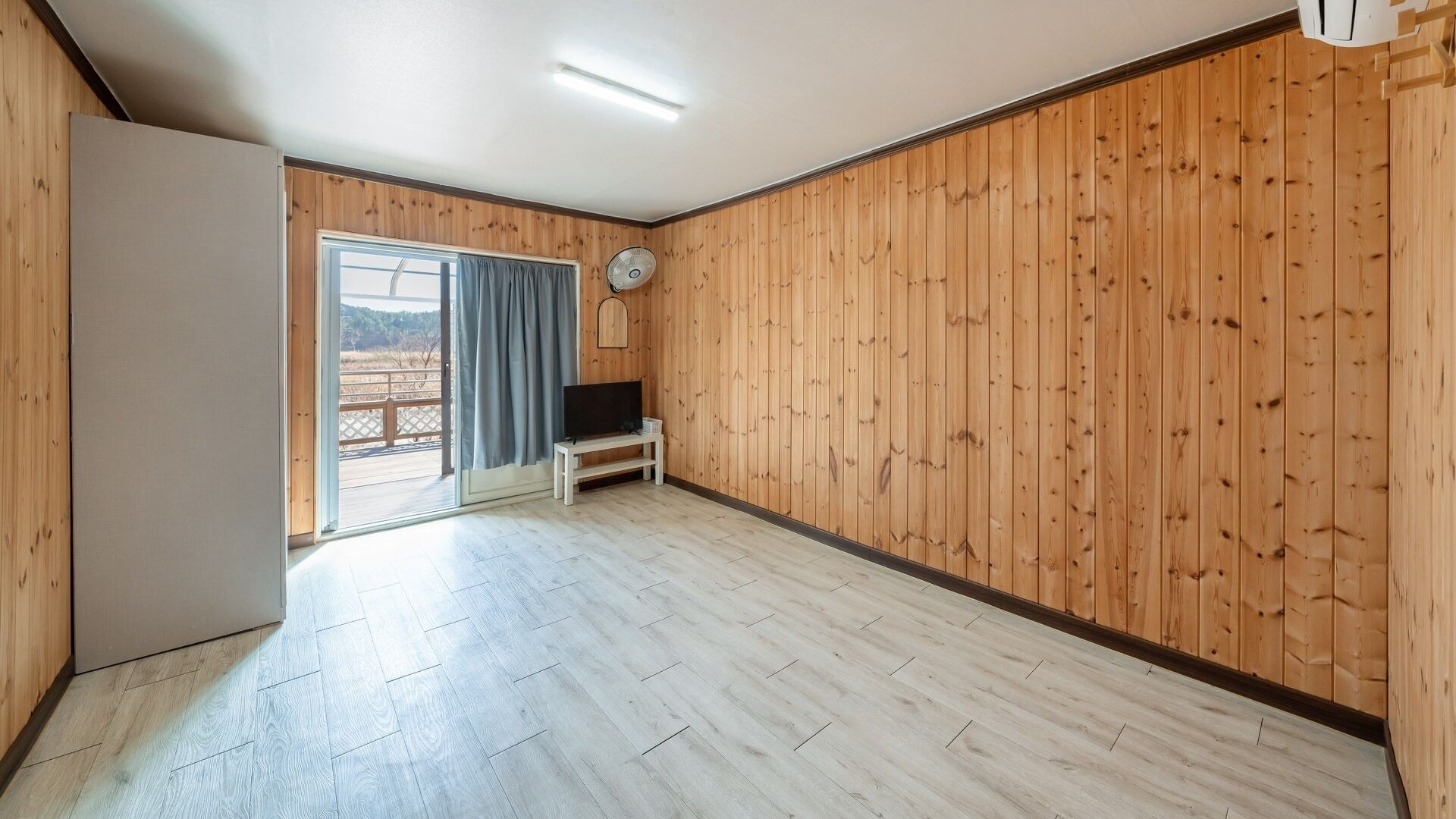 A room with wooden panel walls, a sliding glass door leading outside, a white bench, and a ceiling fan.