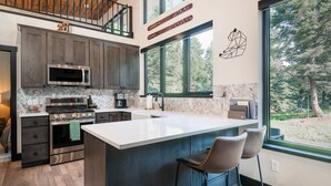 A modern kitchen with a large island, dark wood cabinets, stainless steel appliances, and a view of the forest through large windows. - Romantic, Private Cabin with hot tub and private trail. 7 minutes to Philipsburg (Philipsburg)