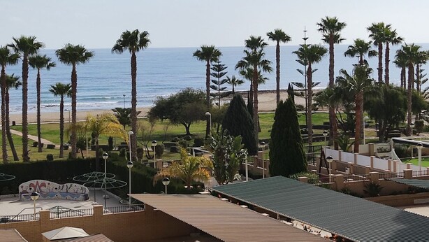 Un hotel frente a la playa con palmeras, arena y vista al océano.