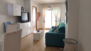 Una sala de estar con sofá color turquesa, un televisor, armarios blancos y una cesta de mimbre.