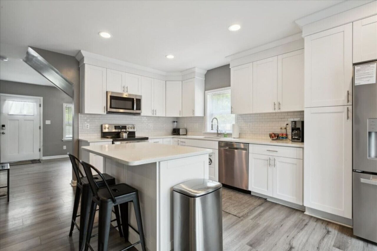 A modern kitchen with white cabinetry, stainless steel appliances, and a central island with bar stools.