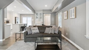 A modern living room with a gray sofa, a glass coffee table, and a kitchen in the background. - Monthly pet-friendly, <5 min walk to beach (Hampton)