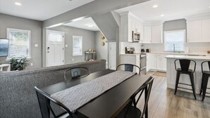 A modern kitchen with white cabinets, a central island, and a dining area with a table and chairs. - Monthly pet-friendly, <5 min walk to beach (Hampton)