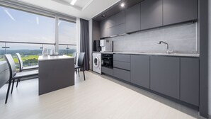 A modern kitchen with grey cabinets, a built-in oven, and a large window overlooking a scenic view. - Gangneung Chonpines Ocean Suites Hotel (Gangneung)