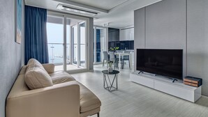 A modern living room with a beige sofa, a flat-screen TV, and a dining area with a table and chairs. - Gangneung Chonpines Ocean Suites Hotel (Gangneung)