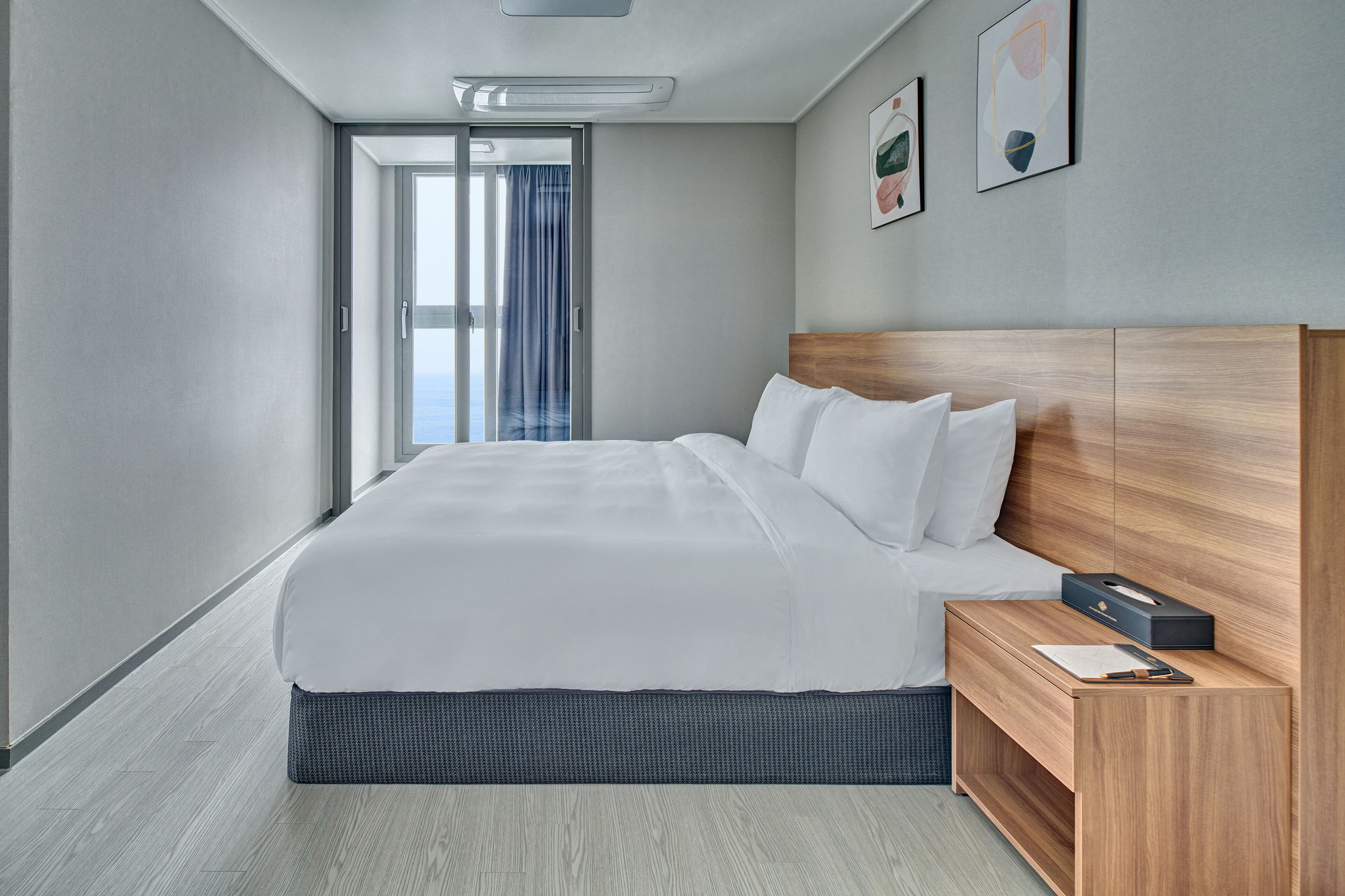 A modern hotel room with a large bed, wooden headboard, and a small bedside table with a lamp.