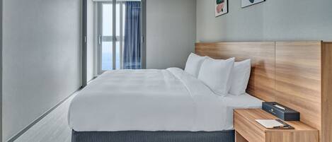 A modern hotel room with a large bed, wooden headboard, and a small bedside table with a lamp.