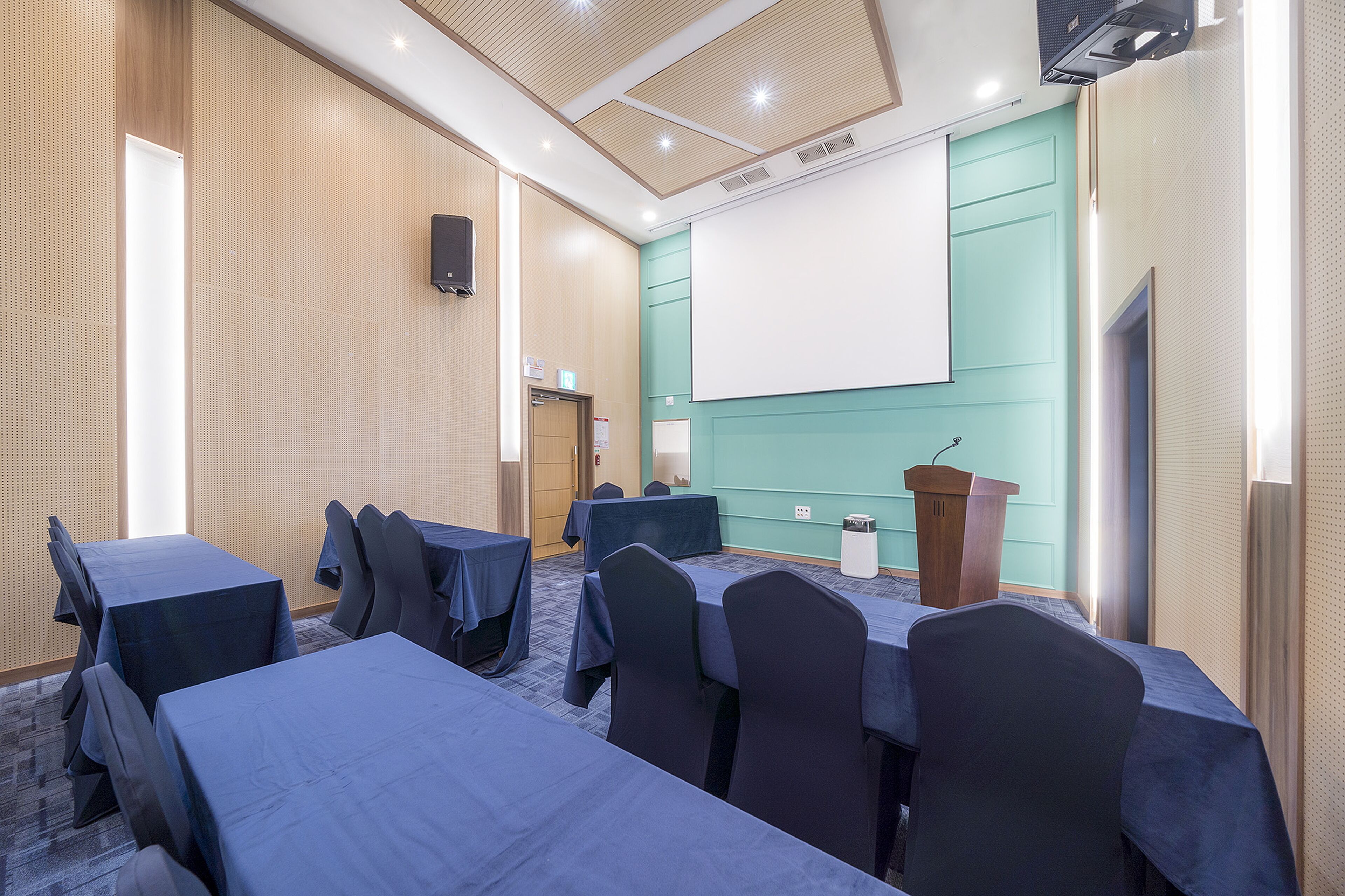 A conference room with tables, chairs, a podium, and a projection screen.