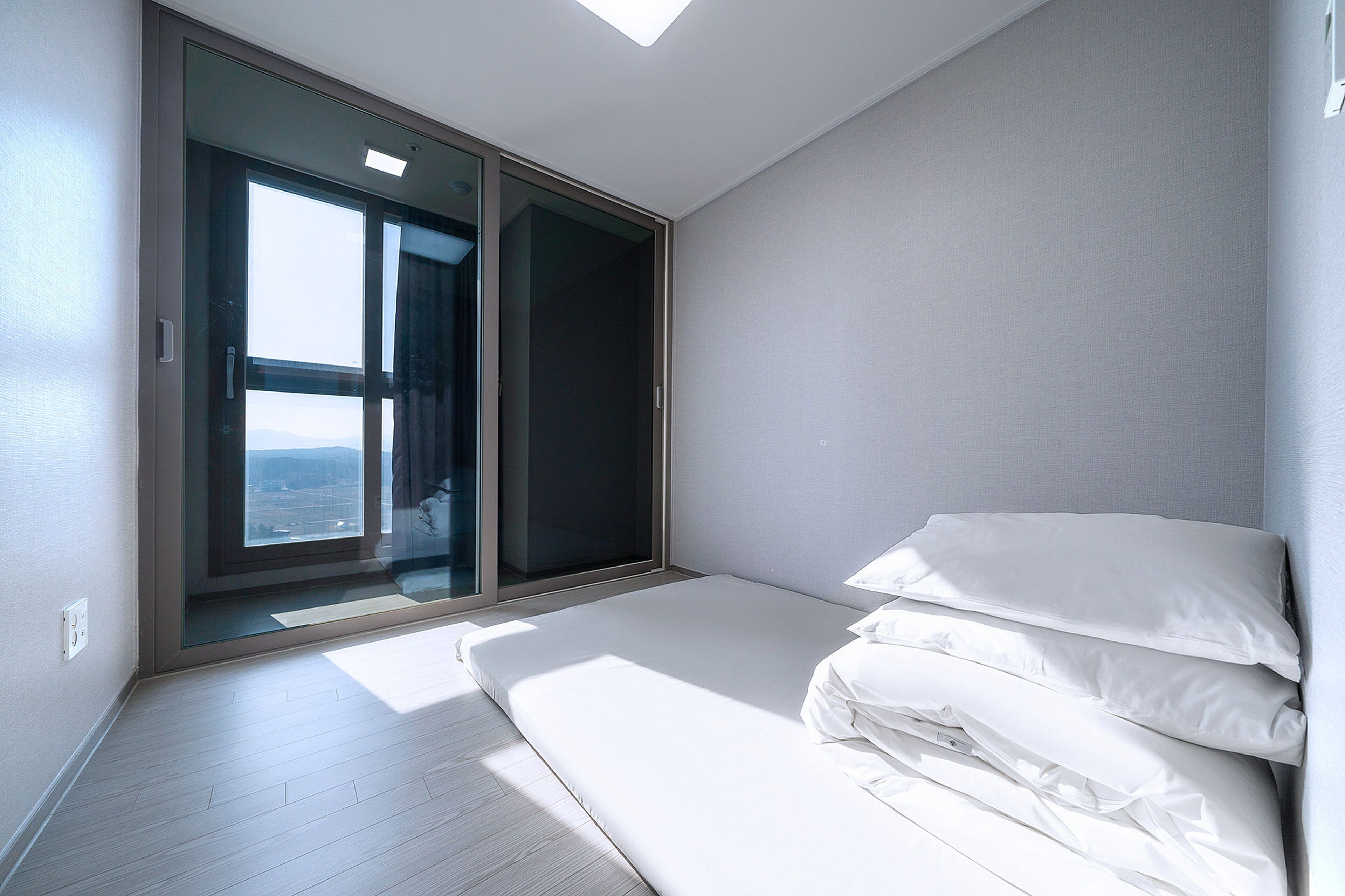 Ein Schlafzimmer mit einer großen Glasschiebetür, die zu einem Balkon führt, einem Bett mit weißen Leinen und einem hellen Holzboden.