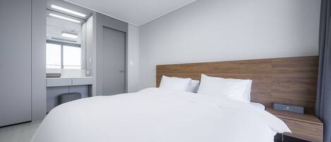 Ein modernes Hotelzimmer mit einem großen Bett, einem Holzkopfstück, einem Nachttisch mit Lampe sowie einem eingebauten Schreibtisch mit Stuhl.