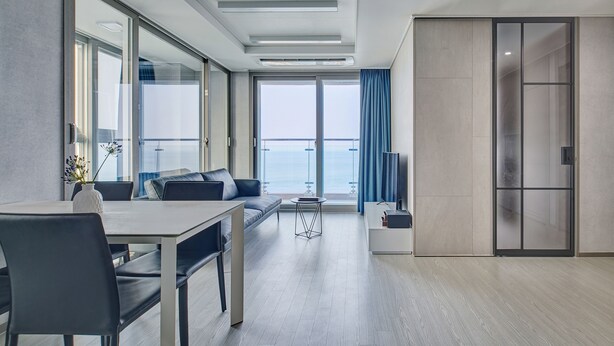 A modern hotel room with a dining area, a sofa, a TV, and a view of the sea. - Gangneung Chonpines Ocean Suites Hotel (Gangneung)