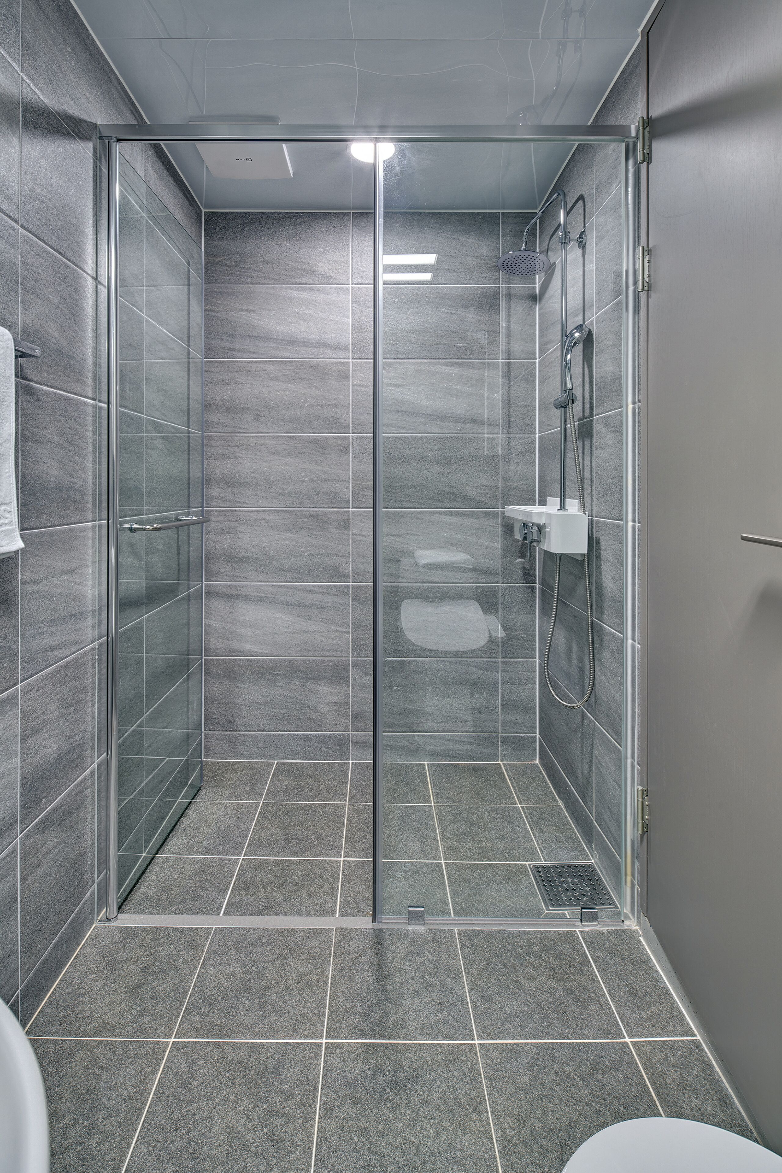 Un espace douche moderne doté d’une porte en verre, d’un pommeau de douche à main et d’un robinet mural.