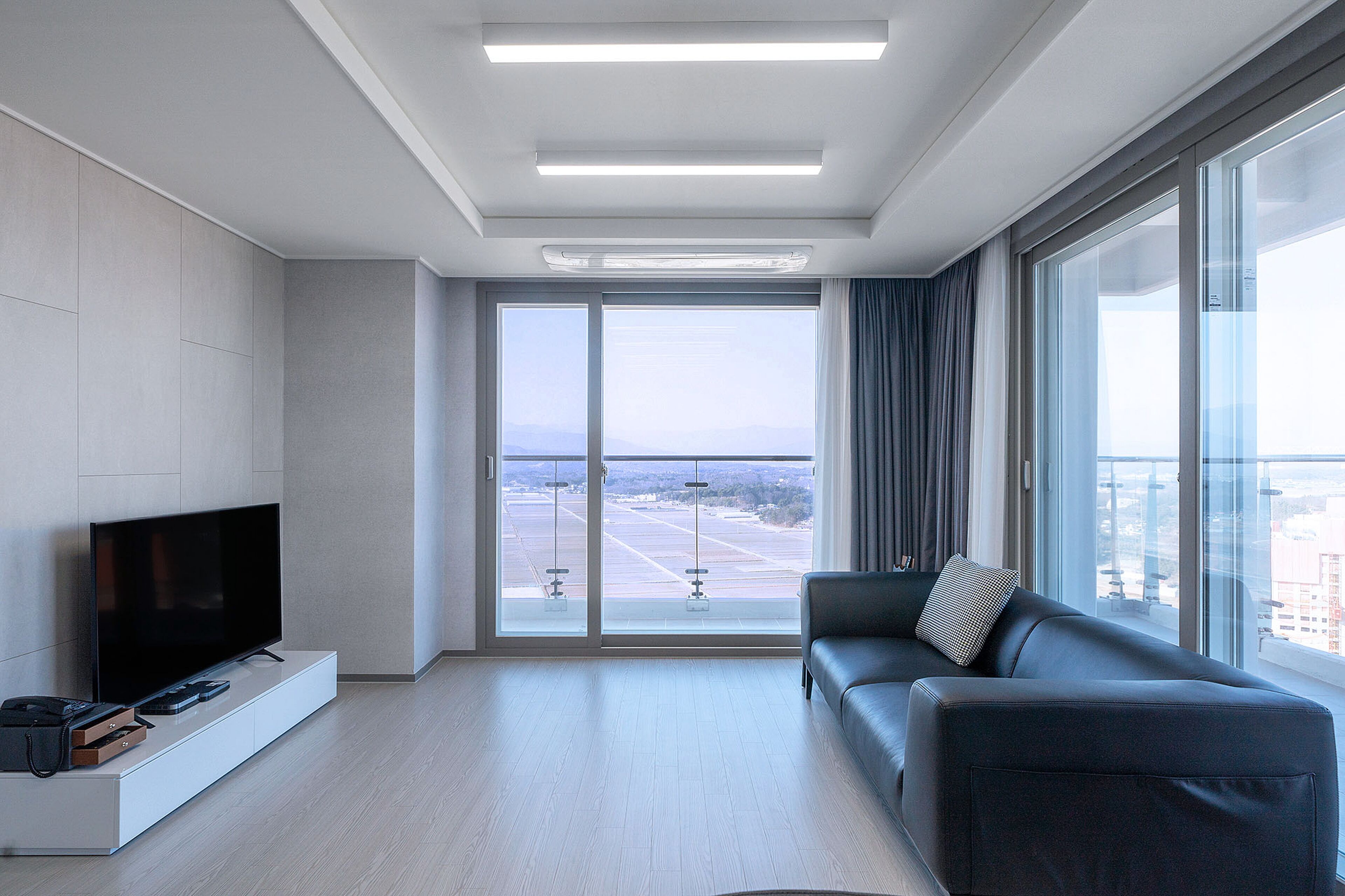 A modern living room with a flat-screen TV, a sofa, and a large window offering a view of a cityscape.