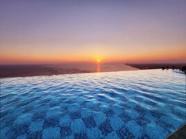 An infinity pool with a view of the sunset over the ocean.
