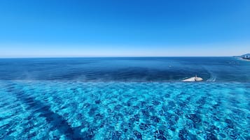 Una vista despejada del océano con un muelle que se adentra en el agua, un barco alejándose de la costa y una línea costera distante con edificios.
