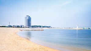 A beach with a lighthouse and a tall building in the background. - Gangneung Chonpines Ocean Suites Hotel (Gangneung)