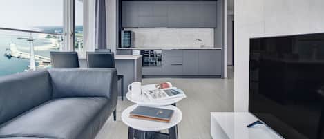 Una sala de estar moderna con un sofá gris, una mesita con una revista y un cuaderno, y un televisor.