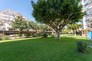 A residential area with a tree in the foreground, a grassy lawn, and a multi-story building in the background. - Apartment 'Acapulco 6' close to the Beach with Shared Pool & Wi-Fi (Fuengirola)