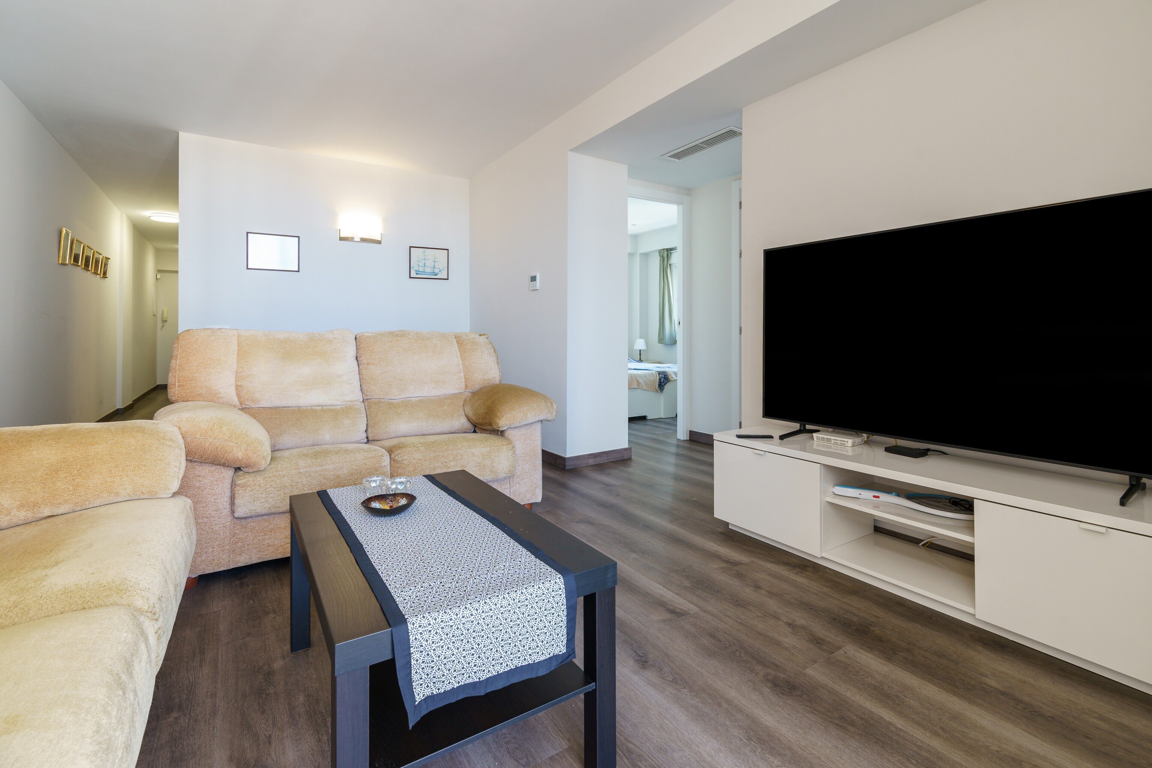 Een woonkamer met een bank, een salontafel, een flatscreentelevisie en een witte tv-meubel.