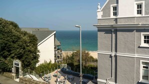 A coastal building with a balcony overlooking the sea, a staircase leading to a door, and outdoor seating. - Jack’s Corner – Sleeps 4 – On-Site Parking – Sea Views – Dog Friendly (St Ives)