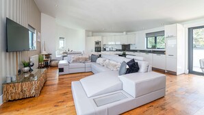 A modern living room with a large sectional sofa, a glass coffee table, and a kitchen area with white cabinets and appliances. - Jack’s Corner – Sleeps 4 – On-Site Parking – Sea Views – Dog Friendly (St Ives)