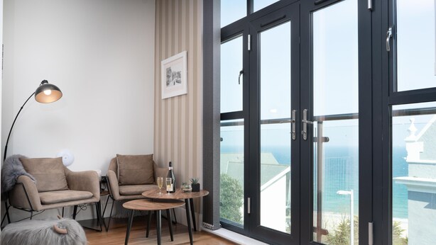 A modern living room with a large window, two sofas, a small round table, and a lamp. - Jack’s Corner – Sleeps 4 – On-Site Parking – Sea Views – Dog Friendly (St Ives)