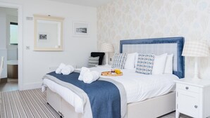 A hotel room with a neatly made bed, a bedside table with a lamp, and a tray with breakfast items. - Jack’s Corner – Sleeps 4 – On-Site Parking – Sea Views – Dog Friendly (St Ives)