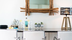 A modern kitchen with white cabinets, a black countertop, and a rustic wooden mirror. There are bar tools, a bottle of gin, and potted plants on the counter. - Jack’s Corner – Sleeps 4 – On-Site Parking – Sea Views – Dog Friendly (St Ives)