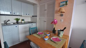 A kitchen with white cabinets, a sink, and a dining table set with plates, bowls, and a bottle of wine. - Charming studio for rent in Roses, Costa Brava. Capacity for 3 people. With terrace, community pool and close to the beach. Book now! (Roses)