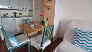 A compact kitchen with white cabinets, a wooden dining table, and chairs. - Charming studio for rent in Roses, Costa Brava. Capacity for 3 people. With terrace, community pool and close to the beach. Book now! (Roses)