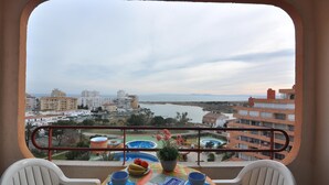 A balcony with a table set for breakfast, overlooking a cityscape and a body of water. - Charming studio for rent in Roses, Costa Brava. Capacity for 3 people. With terrace, community pool and close to the beach. Book now! (Roses)