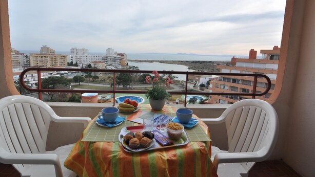 A balcony with a table set for breakfast, overlooking a coastal cityscape. - Charming studio for rent in Roses, Costa Brava. Capacity for 3 people. With terrace, community pool and close to the beach. Book now! (Roses)