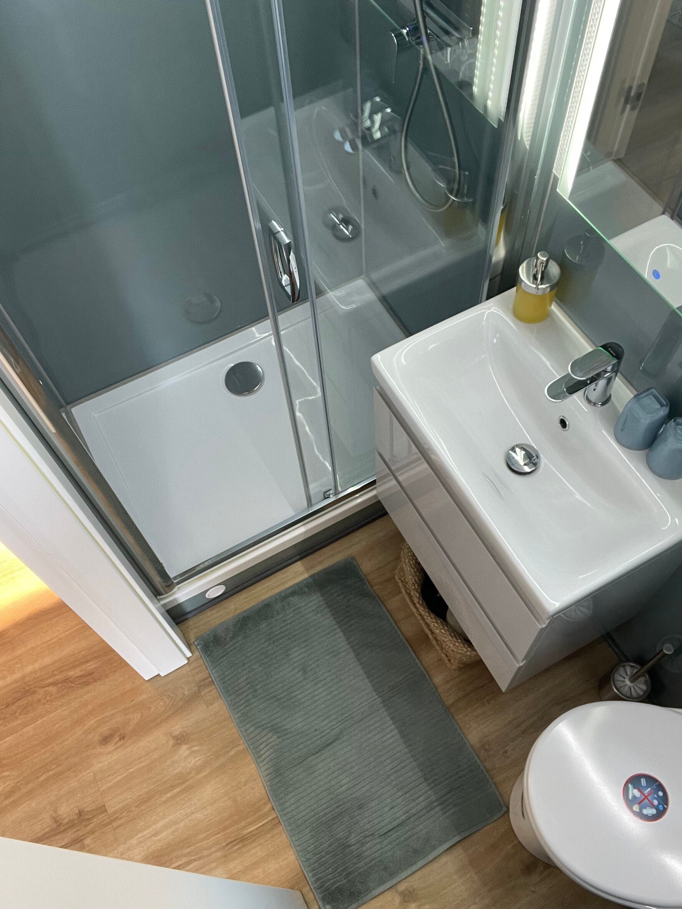 Ein Badezimmer mit Duschkabine aus Glas, Waschbecken mit Spiegel und Toilette.