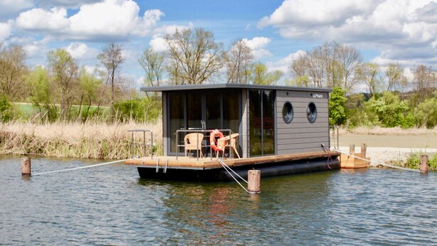 Una casa flotante con terraza, zona de estar y una pequeña estructura con ventanas.