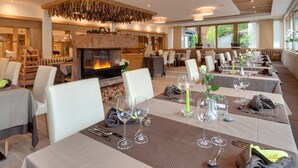 Ein Restaurant mit Kamin, langen Esstischen und weißen Stühlen.