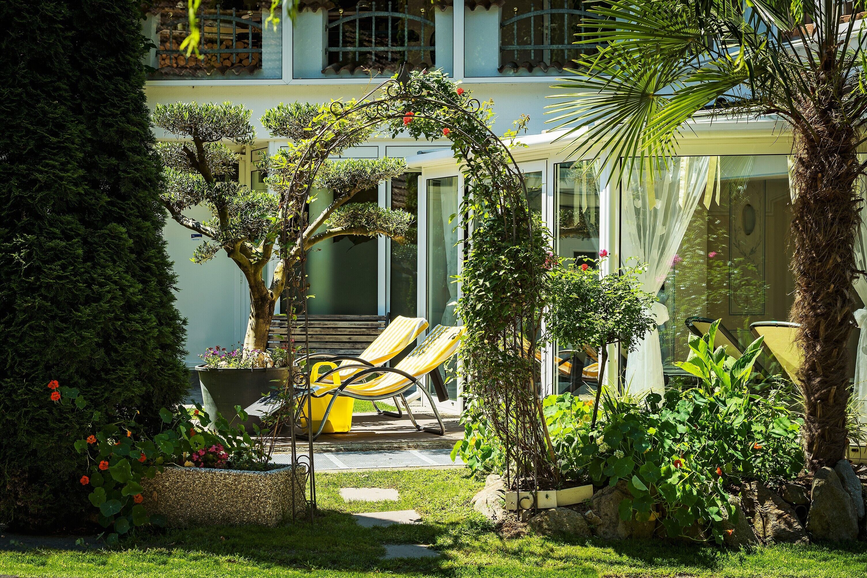 Een verzorgde tuin met diverse planten en een zitgedeelte met gele stoelen.