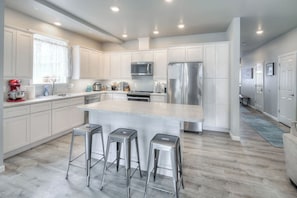 A modern kitchen with white cabinetry, stainless steel appliances, and a central island with stools.