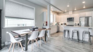 Cocina moderna con armarios blancos, electrodomésticos de acero inoxidable y una mesa de madera con cuatro sillas.