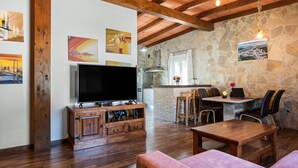 Ein Wohnzimmer mit Fernseher, Holzmöbeln, Steinwänden und einer Essecke mit Stühlen und Tisch.
