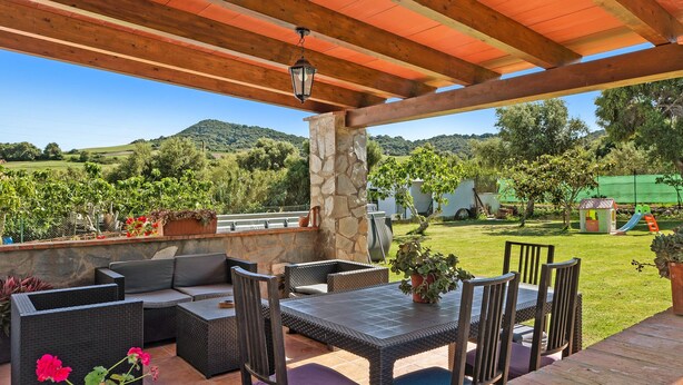 Eine Terrasse im Freien mit Korbmöbeln, einer Stein Säule und Blick auf eine grüne Landschaft.