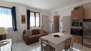 Ein kompakter Wohnbereich mit Sofa, Esstisch, Küchenzeile und einer Wanduhr.