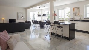 Ein geräumiger Wohnbereich mit einer Couch, einem Esstisch mit Stühlen, einer Küche mit Bar und großen Fenstern.
