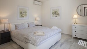 Ein Schlafzimmer mit einem Bett, zwei Nachttischen, einer Kommode, einem Spiegel und zwei Wand-Klimaanlagen.