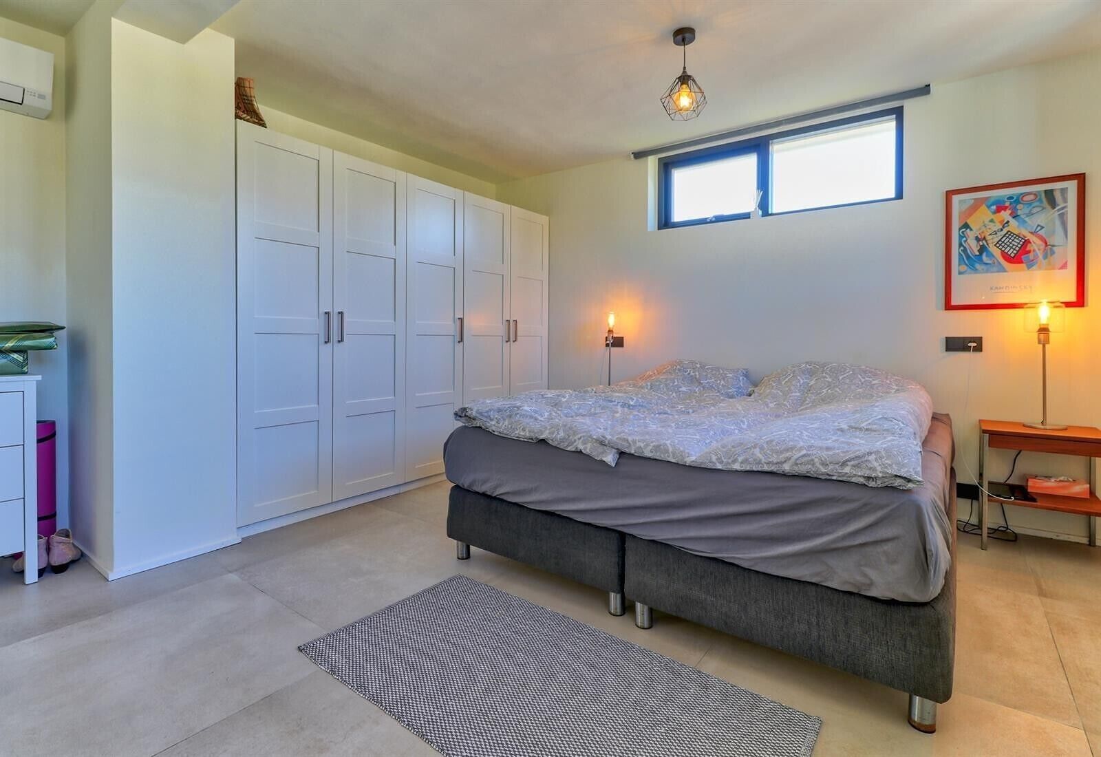 Un dormitorio con cama, armario, mesita de noche, lámpara y una obra de arte.