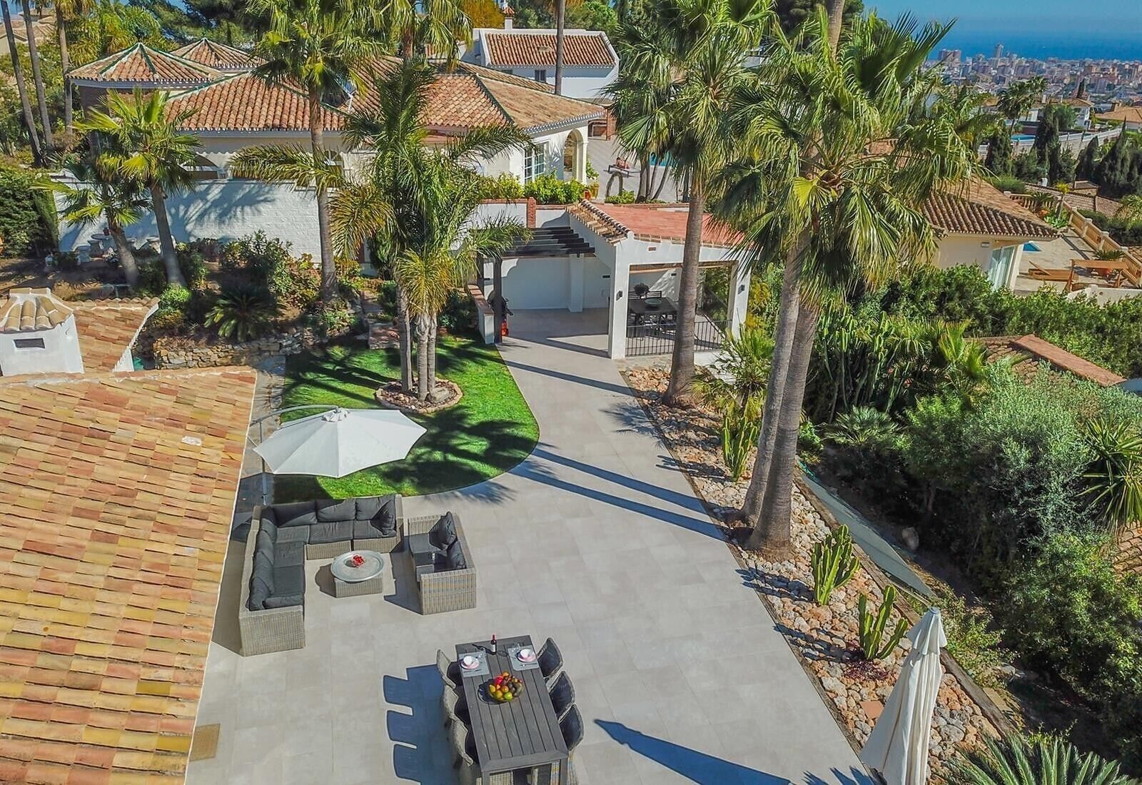 A residential area with a paved driveway, outdoor seating, and palm trees.