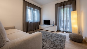 A modern living room with a sofa, a flat-screen TV on a white cabinet, a large rug, and a floor lamp. - Apartment 'Plose 35' in strategic location with Mountain View, Balcony & Wi-Fi (Bressanone)