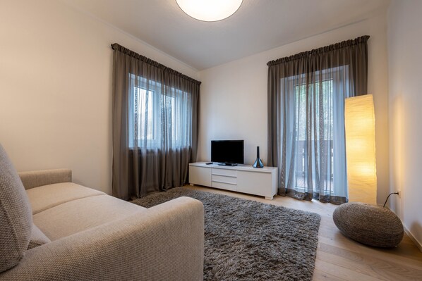 A modern living room with a sofa, a flat-screen TV on a white cabinet, a large rug, and a floor lamp. - Apartment 'Plose 35' in strategic location with Mountain View, Balcony & Wi-Fi (Bressanone)